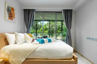 a bedroom with a large white bed with windows at Beachside Residences by NLA in Bang Tao Beach