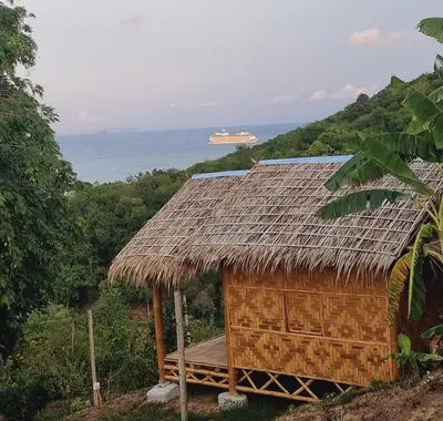 a straw hut with a cruise ship in the background at Sea True Valley Phuket ซี ทรู วัลเลย์ ภูเก็ต in Ban Ao Makham