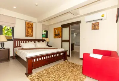 a bedroom with a bed and a red chair at Naiharn beach sands Apartment in Nai Harn Beach