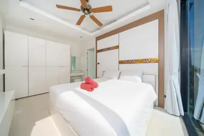 a white bedroom with a white bed and a ceiling fan at Sea & Mountain Views Apartment A602 at VV Patong in Patong Beach