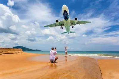 two people on a beach with an airplane flying over them at Студия мечтателя in Mai Khao Beach