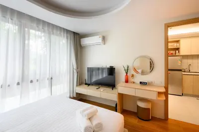 a white bedroom with a bed and a television at Fantasea Kamala Walk to Beach Pool & Gym Modern 1BR in Kamala Beach