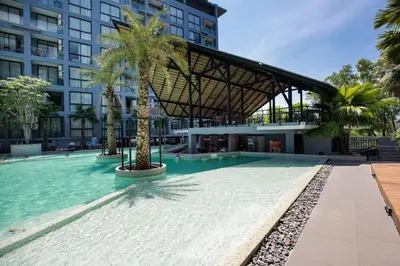 a swimming pool with palm trees in front of a building at Tropics & Modern Stay - Kamala 2BR Suite CTG L502-3, Best Amenities & Beach Fun in Kamala Beach