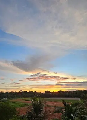 a sunset in a field with trees and a sky at Lovely Mai Khao studio room in Mai Khao Beach