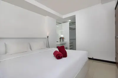 a white bed with a red pillow on it at Rawai Apartment RBC 311, near Famous Rawai Market in Phuket Town