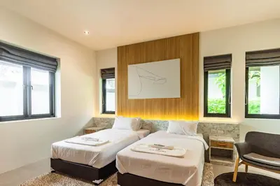 a hotel room with two beds and a chair at Bangtao Beach Walk Villa by Taan Residence in Bang Tao Beach