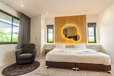 a bedroom with a bed and a chair and a mirror at Bangtao Beach Walk Villa by Taan Residence in Bang Tao Beach