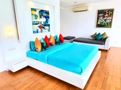 a white room with a blue bed with colorful pillows at Beautiful Modern Penthouse Kamala Beach in Kamala Beach