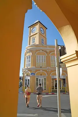 two people walking in front of a building with a clock tower at xx Mitr INN Phuket Oldtown - มิตร ภูเก็ต in Phuket Town