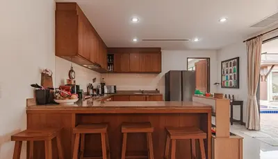 a kitchen with wooden cabinets and a counter with stools at 4 BR Jacuzzi Pool Villa with Playground, near Layan, Laguna, Bang Tao beach in Ban Pak Lak