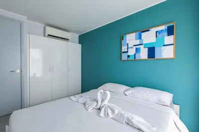 a bedroom with a white bed with a blue wall at Pool View 1 Bed Apt T2-720 in Chalong