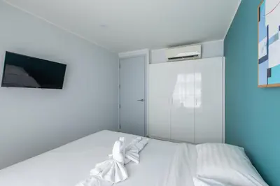 a bedroom with a bed with white sheets and a tv at Pool View 1 Bed Apt T2-720 in Chalong