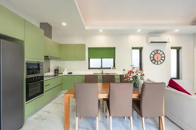 a kitchen with green cabinets and a wooden table and chairs at V193 Next-Door Villas 6BR 2 Pools For Group Vibe! in Rawai Beach