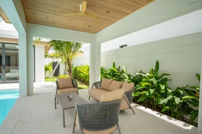 a patio with chairs and a table next to a pool at Mouana Breeze Maikhao 3-bedroom Pool Villa 9917 in Mai Khao Beach