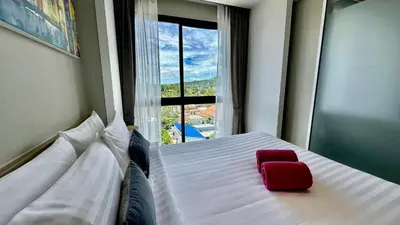 a red chair sitting on a bed in a room with a window at Apartment Diamond Resort BangTao in Bang Tao Beach
