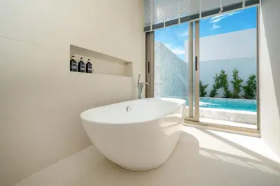 a bathroom with a large white tub in front of a window at The Trinity new modern 5BR villa with 20M Pool in Thalang