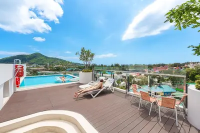 a woman sitting on a deck with a view of a pool at C190 Sleek 1BR with Infinity Pool, Gym, Rooftop in Kamala Beach