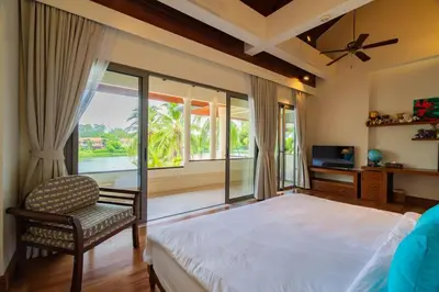 a bedroom with a bed and a chair and windows at 4BR Lakeshore Pool Villa in Laguna Bangtao in Bang Tao Beach