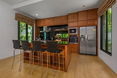 a kitchen with wooden cabinets and a bar with stools at Villa Fam with Private Pool Near Nai Harn Beach in Rawai Beach