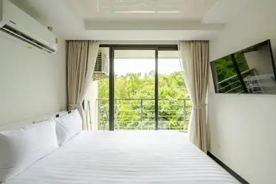 a bedroom with a white bed with a balcony at Room 402 Rawai Beach Condo in Nai Harn Beach