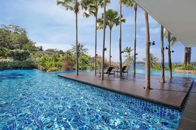 a swimming pool with palm trees and a wooden deck at Stunning Seaview Escape - Modern and Elegant in Kata Beach