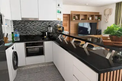 a kitchen with white cabinets and a black counter top at Cozy Retreat Near Beach and Pools in Kamala Beach