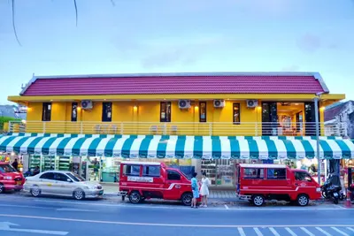 a yellow building with cars parked in front of a store at Bed & Beach Hostel Karon in Karon Beach