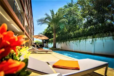a swimming pool next to a building with a table and flowers at Rawai Beach - 1 BR Cozy Condo in Nai Harn Beach