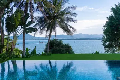 a swimming pool with palm trees and a view of the water at Villa Serenity -30 meter Pool & 6 Bedroom with Cinema Room and Gym in Ko Lek