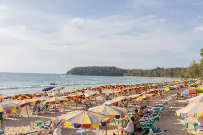 a group of people sitting on a beach with umbrellas at Kata Palace Phuket Hotel in Kata Beach