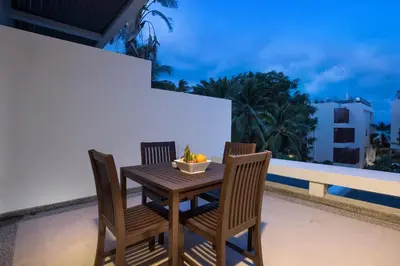 a wooden table and chairs on a balcony at Tropical Serenity - Elegant 1 Bedroom with Pool in Ban Saiyuan (1)