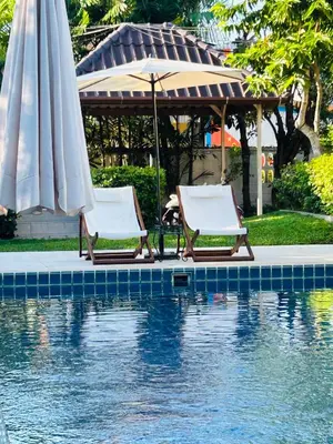 two lounge chairs and an umbrella next to a pool at Green View suite with private bathroom and kitchen in Ban Phlu Yai
