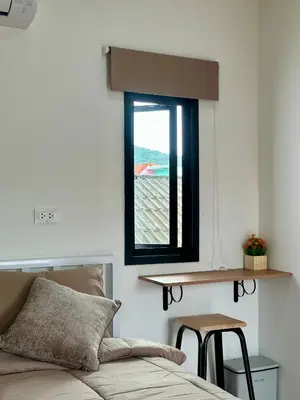 a bedroom with a window and a bed and a stool at Bike Works Inn Bang Tao in Ban Thalat Choeng Thale