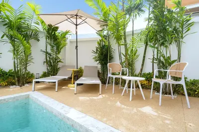 a patio with chairs and an umbrella next to a pool at Goldena Residence Private Pool Villas in Kamala Beach