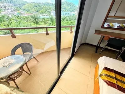 a room with a balcony with a bed and a table at Patong Leisure Hotel in Patong Beach