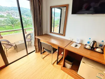 a room with a desk with a view of a balcony at Patong Leisure Hotel in Patong Beach