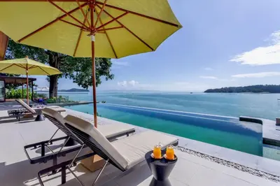 a pool with chairs and an umbrella and the water at Villa Eugenia in Phuket Town