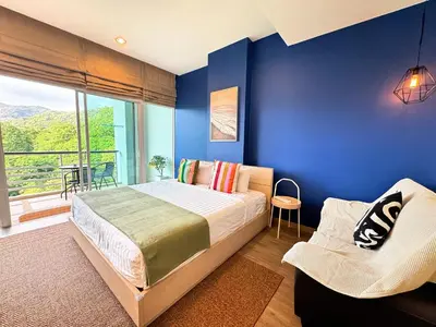 a bedroom with blue walls and a bed and a chair at Veloche Peaceful Condo In Karon Beach in Karon Beach