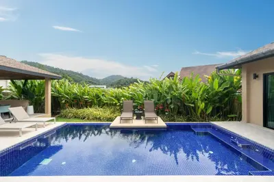 a swimming pool with two lounge chairs next to a house at Naiharn Beach 4 Bedroom Villa in Nai Harn Beach