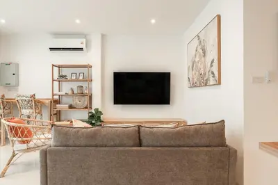a living room with a couch and a tv on a wall at Nai Harn Beach Holiday Home - Rawai in Rawai Beach