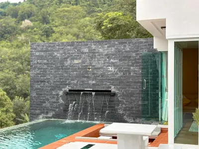 a swimming pool with a stone wall and a fountain at The Eden Hill in Phuket Town