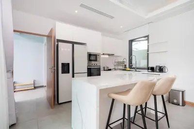 a kitchen with white counters and two stools at Luxury 3BR Pool Villa Relaxation in BangTao Laguna in Laguna Phuket