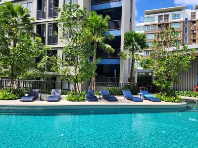 a swimming pool with blue lounge chairs in front of a building at Cozy Palm Haven apartment in Kathu