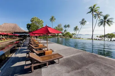 a row of chairs and umbrellas next to a body of water at The Vijitt Resort - Deluxe Beachfront Villa in Ban Saiyuan (1)