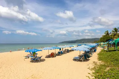 a beach with many blue umbrellas and people on it at Spacious studio with access to the pool in Karon Hill condo in Karon Beach