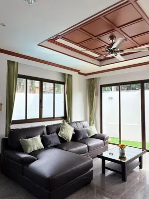 a living room with a black leather couch and windows at RisaVilla Phuket - 4BR Pool Villa near Patong Beach in Patong Beach