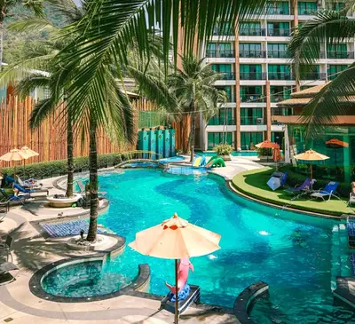 a pool with an umbrella and palm trees and a building at Stay Kata in Kata Beach