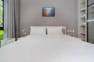 a bedroom with a white bed and a painting on the wall at Apartments 15 minutes walk from Bangtao Beach with a cinema in Phuket