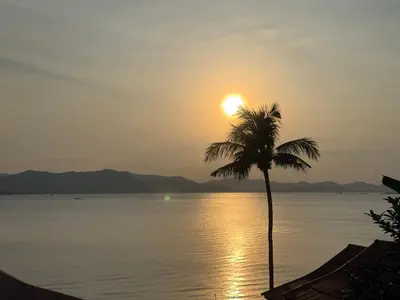 a palm tree in front of the ocean at sunset at The Good View Koh Yao Noi in Ko Yao Noi