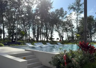 a swimming pool with white chairs in a park at Kora Beach Resort Phuket in Bang Tao Beach